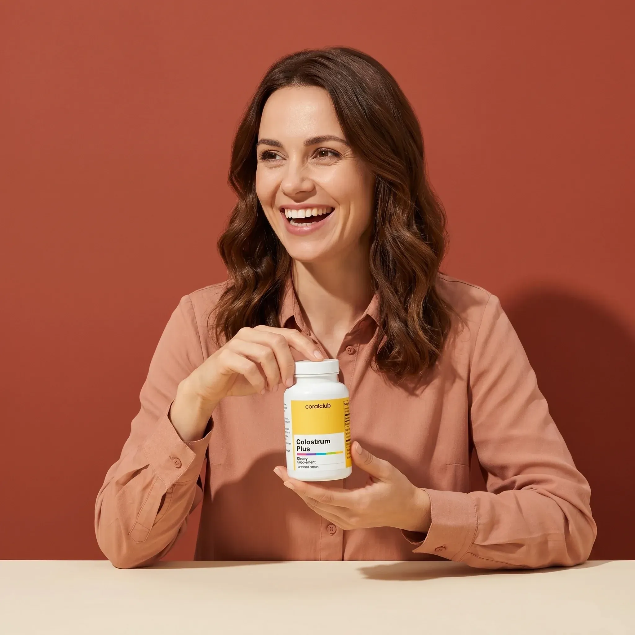 Woman holding Colostrum Plus supplement bottle against a warm background, smiling.