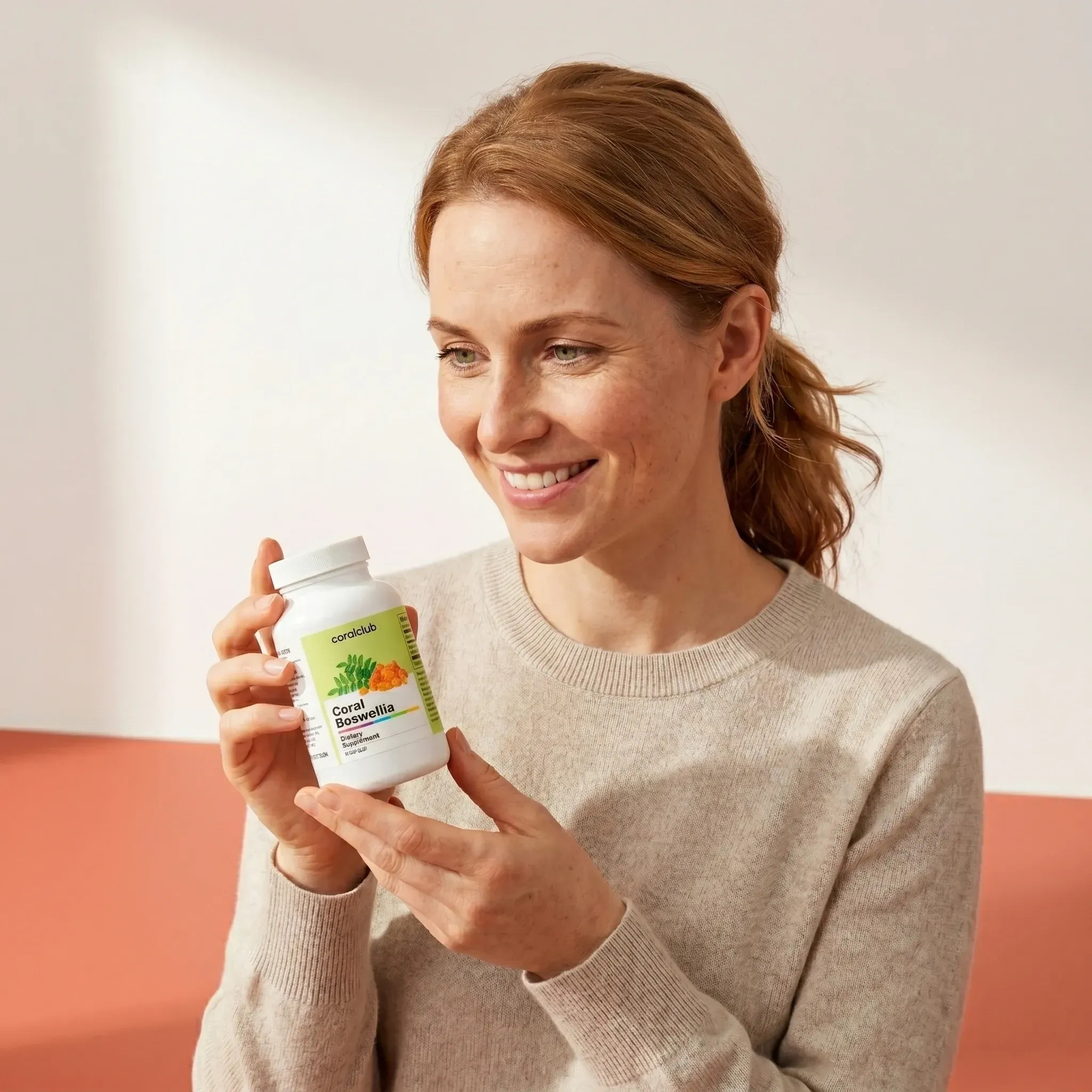 Woman smiling while holding a bottle of Coral Boswellia dietary supplement in a bright lifestyle setting.
