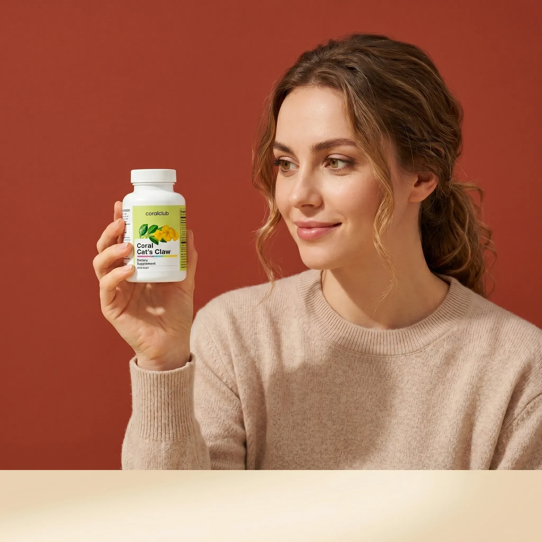 Woman holding Coral Cat's Claw supplement bottle against a warm background, wearing a cozy sweater.