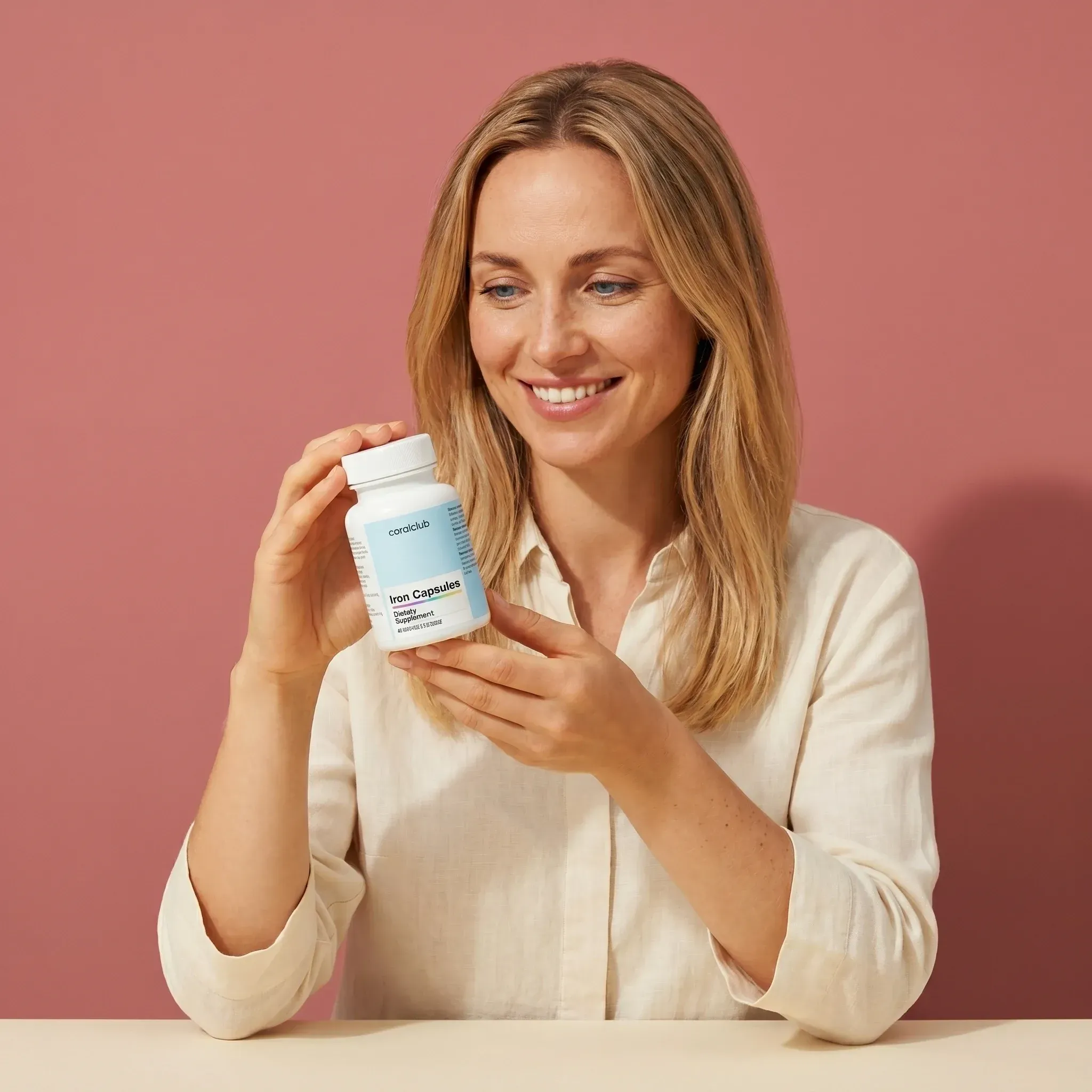 Woman holding a bottle of Iron supplement against a pink background.